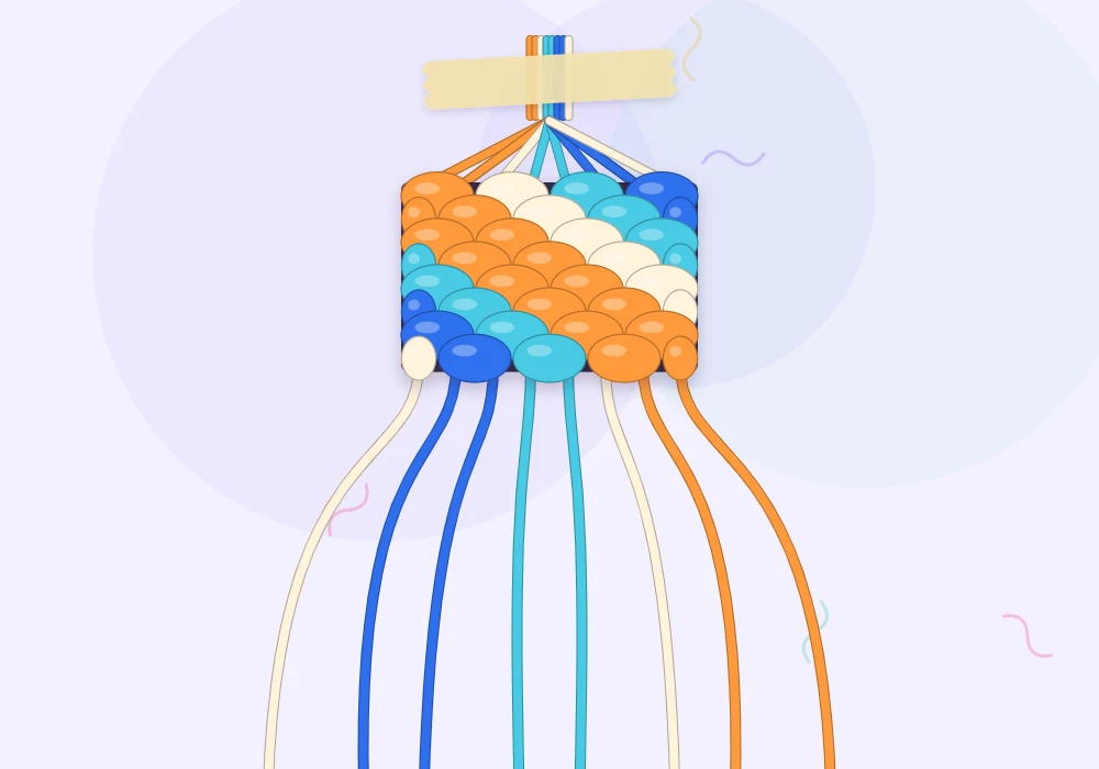 A candy stripe bracelet in progress taped at the top, with tangerine, cream, aqua and cobalt diagonal stripes and loose strings fanned out below