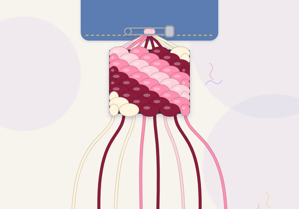 A diagonal stripe bracelet in progress held by a pin, with a thin blush line, a rose stripe, a wide burgundy band and a cream stripe